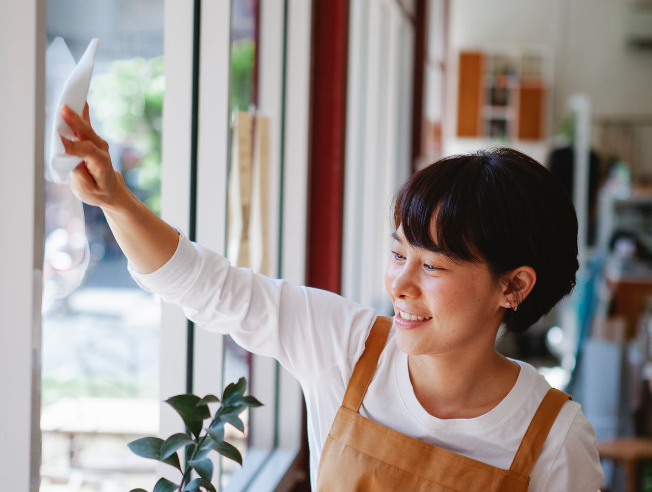 about-01 Smiling woman in apron wipes glass window at a small business. Indoor shot.